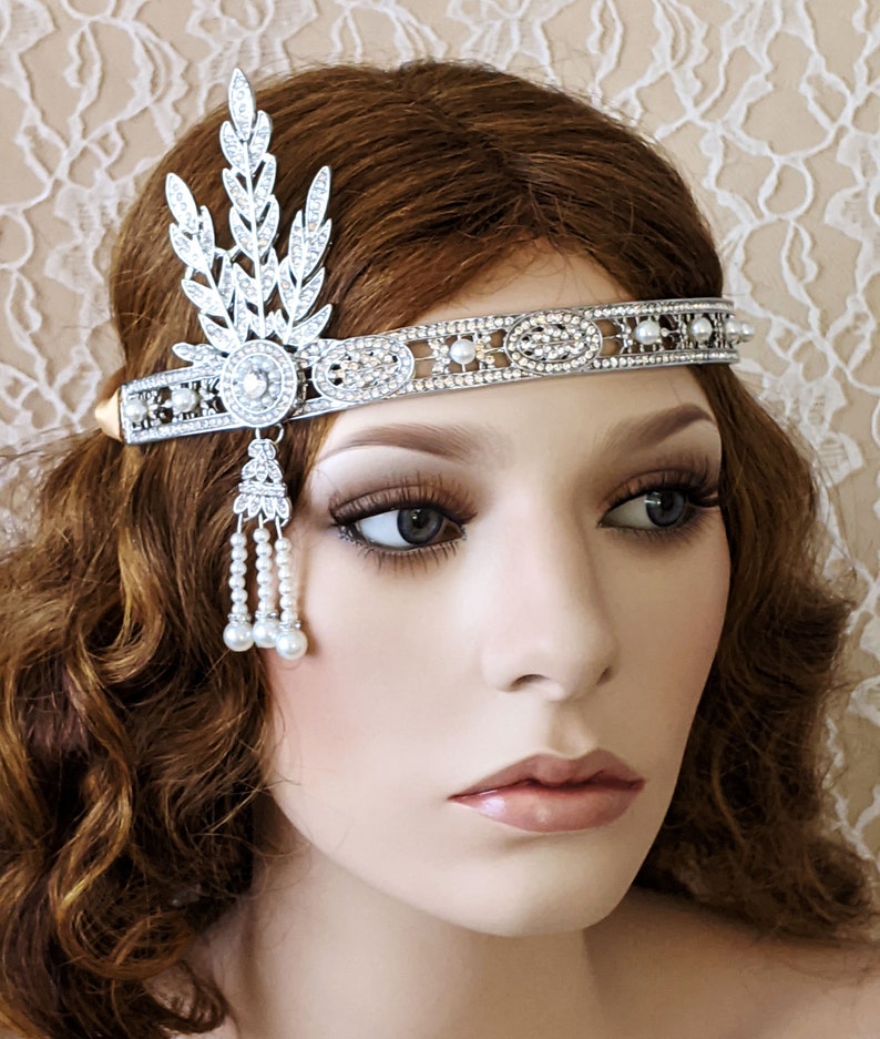 May include: A silver headband with a pearl and rhinestone design. The headband has a leaf-shaped design on one side and a row of pearls and rhinestones on the other side.
