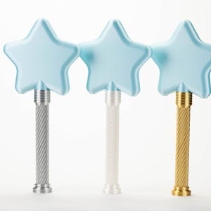 Peut inclure: Trois baguettes magiques en forme d'&eacute;toile avec des dessus bleu clair et des manches textur&eacute;s. Une baguette a une poign&eacute;e argent&eacute;e, une est blanche et la troisi&egrave;me est dor&eacute;e. Les baguettes sont sur fond blanc.