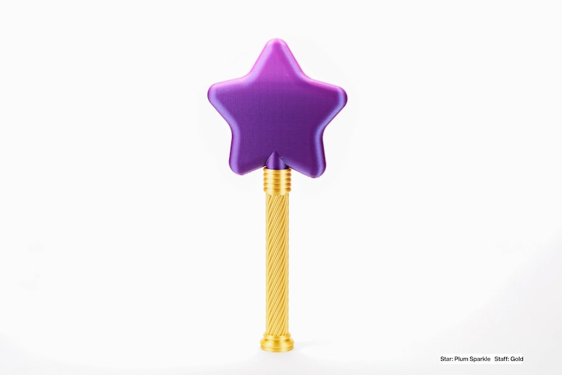 Peut inclure: Une baguette magique en forme d'&eacute;toile violette avec un manche dor&eacute;. L'&eacute;toile est de couleur prune fonc&eacute;e et le manche a un design torsad&eacute;. L'objet est sur le th&egrave;me de la magie.