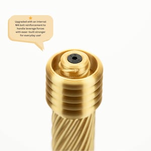 Peut inclure: Gros plan d'un objet cylindrique dor&eacute; avec un design textur&eacute; et nervur&eacute;. Le dessus pr&eacute;sente un motif circulaire avec un centre noir. Le texte dans une bulle indique : "Upgraded with an internal M4 bolt reinforcement to handle leverage forces with ease-built stronger for everyday use!"