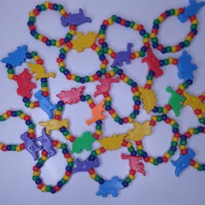 May include: Colorful beaded bracelets with dinosaur-shaped charms. The beads are red, yellow, green, blue, and purple. The dinosaur charms are in various colors, including red, yellow, blue, green, orange, and purple. These bracelets are a fun accessory.