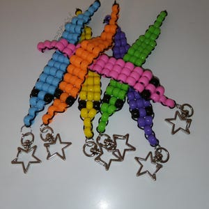 May include: A collection of colorful beaded bracelets in blue, orange, yellow, green, pink, and purple. Each bracelet has a star-shaped charm attached. The bracelets are made of small, round beads.