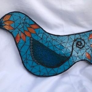 May include: A blue mosaic bird with orange accents. The bird is made of small pieces of glass and tile.