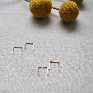 May include: Two sets of small, silver and gold, hoop earrings. The hoops are open and have a square shape.