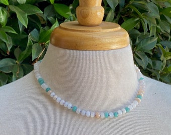 May include: A delicate necklace made with white, light blue, and peach colored beads. The necklace is on a white mannequin.