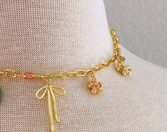May include: A gold chain necklace with multiple charms, including a bow, a flower, and a small animal. The necklace is on a white mannequin.