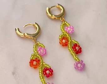 May include: A pair of gold hoop earrings with dangling beaded flower charms. The charms are made of green, pink, orange, and red beads.