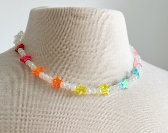 May include: A rainbow star necklace with white beads. The necklace is made of plastic and has a rainbow of colors, including red, orange, yellow, green, blue, and purple.