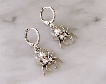 May include: A pair of silver hoop earrings with a dangling spider charm. The spiders have a detailed design and are a fun and spooky accessory.