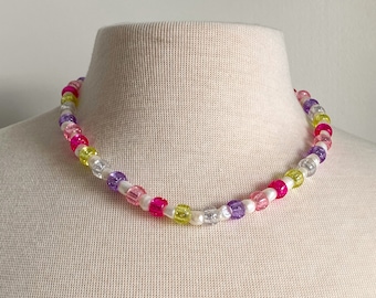 May include: A colorful beaded necklace with pink, purple, white, and yellow beads. The beads are translucent and have a slightly iridescent finish.