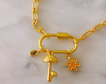 May include: Gold chain necklace with a gold carabiner clasp and three charms: a green gemstone, a gold mushroom, and a gold flower with orange crystals.