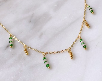 May include: A gold chain necklace with green and white beads hanging from it. The beads are arranged in a striped pattern.
