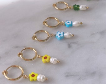 May include: Five pairs of gold hoop earrings with dangling charms. Each charm features a different colored flower with a pearl bead. The flowers are yellow, blue, green, and red.