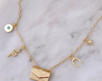 May include: Gold chain necklace with multiple charms, including a snake, horseshoe, star, and a small envelope charm. The envelope charm has an intricate design.