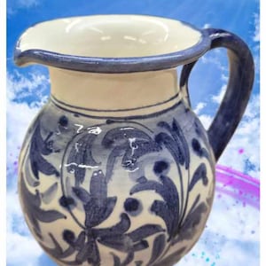 Könnte beinhalten: Ein Keramikkrug mit cremefarbener Basis und handgemalten dunkelblauen Blumenmustern. Der Krug verfügt über einen breiten Ausguss, einen geschwungenen Henkel und den Schriftzug Le mie ceramiche in Weiß am unteren Rand.