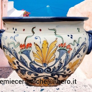 Könnte beinhalten: Ein großer Keramikübertopf mit cremefarbener Basis, verziert mit handgemalten blauen, gelben und orangefarbenen Blumen- und Rankenmotiven. Das Gefäß hat einen breiten Rand, zwei seitliche Griffe und den Text Lemieceramiche@libero.it unten.