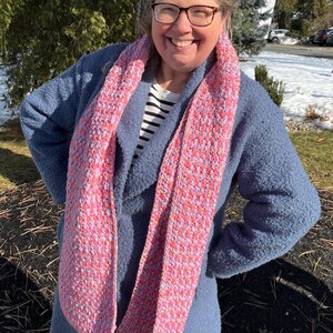 May include: A woman wearing a blue coat with a pink and purple scarf. The scarf has a speckled pattern.