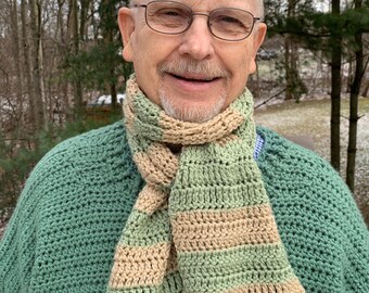 May include: A man wearing a green sweater and a striped crocheted scarf. The scarf is made with green and beige yarn.
