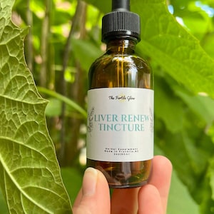 May include: A brown glass bottle with a black dropper, labeled "Liver Renew Tincture" by The Fertile Glow. The bottle is held against a backdrop of green leaves. The label also states "Herbal Supplement" and the bottle contains 2 fl oz / 60ml.
