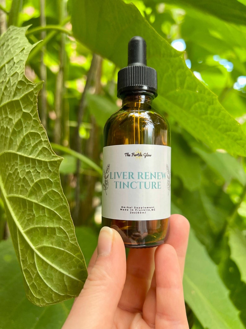 May include: A brown glass bottle with a black dropper, labeled "Liver Renew Tincture" by The Fertile Glow. The bottle is held against a backdrop of green leaves. The label also states "Herbal Supplement" and the bottle contains 2 fl oz / 60ml.