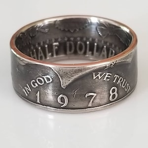 Puede incluir: Un anillo de plata hecho de una moneda de medio dólar de 1978. El anillo presenta las inscripciones "IN GOD WE TRUST" y "HALF DOLLAR". El año "1978" es visible en la superficie del anillo.