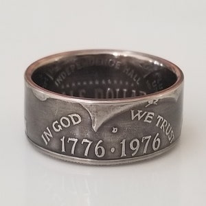 Può includere: Anello d'argento con le iscrizioni "IN GOD WE TRUST" e le date "1776-1976". L'interno dell'anello mostra "INDEPENDENCE HALL". Il design dell'anello è dettagliato e vintage.