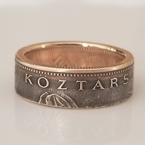 May include: A gold and silver ring with the word "KOZTARS" engraved on the band. The ring has a mountain design and a gold interior. The ring is likely a piece of jewelry.