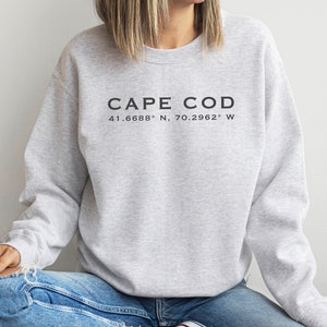 May include: Gray sweatshirt with the text "CAPE COD 41.6688° N, 70.2962° W" printed on the front.