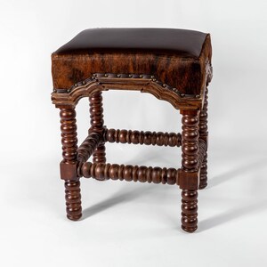 K&ouml;nnte beinhalten: Ein brauner Leder- und Holzhocker mit einem einzigartigen Design. Der Hocker hat eine abgerundete Oberseite und eine Basis mit einer Reihe von Holzperlen.