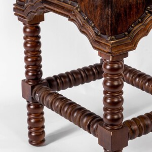 K&ouml;nnte beinhalten: Ein Hocker aus Holz mit einem braunen Ledersitz und gedrehten Beinen. Der Hocker hat ein dekoratives Design an der Ober- und Unterseite der Beine.