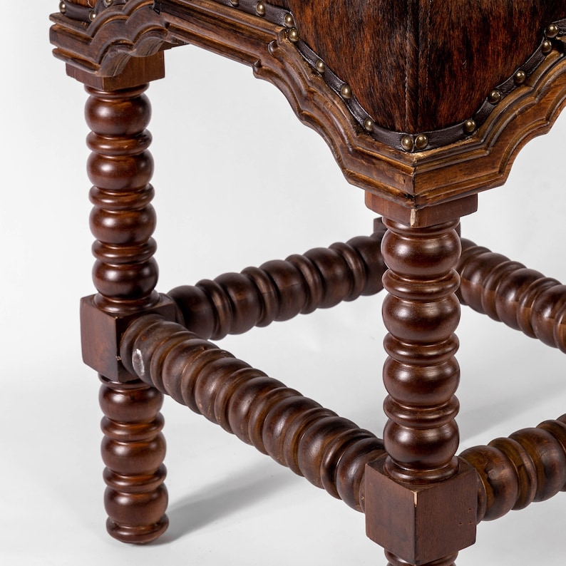K&ouml;nnte beinhalten: Ein Hocker aus Holz mit einem braunen Ledersitz und gedrehten Beinen. Der Hocker hat ein dekoratives Design an der Ober- und Unterseite der Beine.