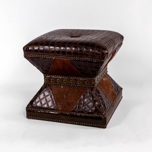 K&ouml;nnte beinhalten: Ein brauner Lederhocker mit quadratischer Oberseite und Rautenmuster. Der Hocker hat eine einzigartige Sanduhrform und ist mit Metallnieten verziert.