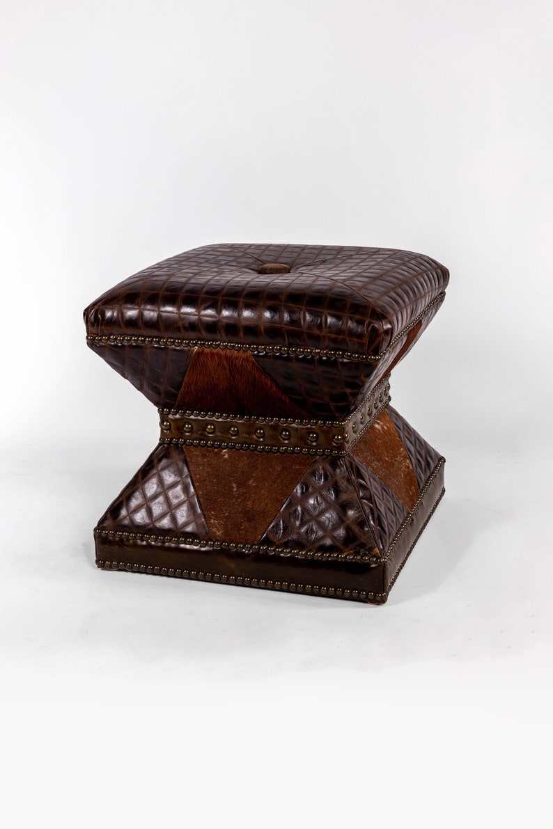 K&ouml;nnte beinhalten: Ein brauner Lederhocker mit quadratischer Oberseite und Rautenmuster. Der Hocker hat eine einzigartige Sanduhrform und ist mit Metallnieten verziert.