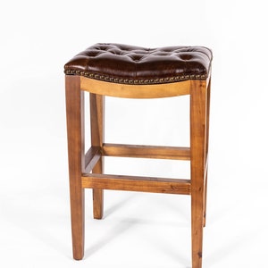 May include: A brown leather bar stool with a tufted seat and a wooden frame. The stool has a curved seat and a footrest.