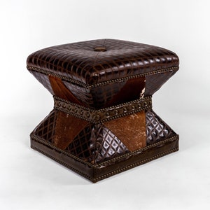 K&ouml;nnte beinhalten: Ein brauner Lederhocker mit quadratischer Oberseite und einem einzigartigen, geometrischen Design. Der Hocker besteht aus verschiedenen Ledersorten, darunter ein braunes Leder mit Kroko-Muster und ein braunes und wei&szlig;es Kuhfellmuster.