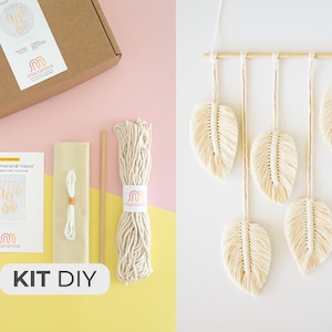 Peut inclure: Un kit de bricolage pour réaliser une suspension murale en macramé avec cinq formes de plumes blanches. Le kit comprend du cordon de coton naturel, une baguette en bois et des instructions. La suspension murale finie est présentée à droite de l'image.