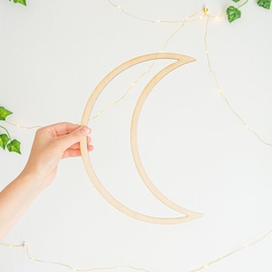 May include: A wooden crescent moon shape wall decoration. The moon is made of light brown wood and is hanging on a white wall.
