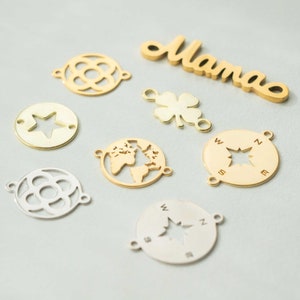 May include: A collection of gold and silver metal charms, including a star, a compass, a clover, a globe, a flower, and a word charm that says "Mama".