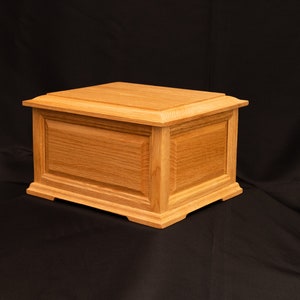 May include: A wooden box with a light brown finish. The box has a simple, rectangular design with a raised lid and a smooth surface.