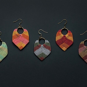 May include: Five pairs of colorful, handmade macrame earrings with a geometric design. Each pair features a different color combination, including pink, orange, green, gray, and brown.