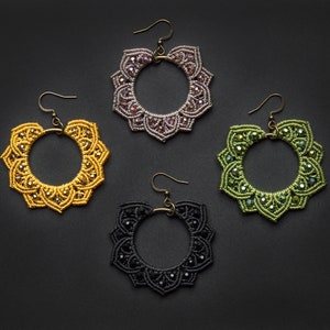 Puede incluir: Cuatro pares de pendientes de ganchillo hechos a mano con un diseño circular. Los pendientes son de cuatro colores diferentes: amarillo, verde, morado y negro.