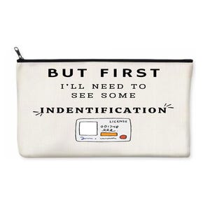 May include: White zippered pouch with black trim. The pouch has black text that reads "BUT FIRST I'LL NEED TO SEE SOME INDENTIFICATION" with a hand-drawn illustration of a driver's license.