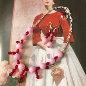 May include: A pink and red beaded necklace and earrings set. The necklace has pink round beads with red crystal accents. The earrings are dangle earrings with pink round beads and red crystal accents.