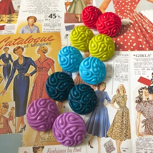 May include: Assortment of colourful patterned buttons with a swirl design. The buttons are in shades of red, yellow, blue, green, and purple.