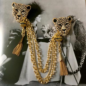 Könnte beinhalten: Ein Paar goldfarbene Broschen mit Leopardkopf, schwarzen Akzenten und herabhängenden Ketten mit goldenen Quasten.