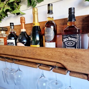 K&ouml;nnte beinhalten: Wandmontiertes Holzregal mit einem Schild mit der Aufschrift "Cocktails" und sechs Weingl&auml;sern, die darunter h&auml;ngen. Das Regal enth&auml;lt sechs Flaschen Alkohol, darunter Jack Daniels, Kraken Rum und eine Flasche Champagner.