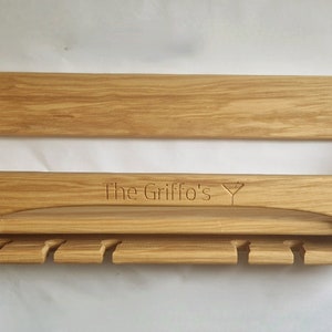 K&ouml;nnte beinhalten: Ein Wand-Weinglashalter aus Holz mit einer personalisierten Inschrift "The Griffo's" und einem Weinglas-Symbol. Der Halter hat ein Regal und eine Reihe von Haken zum Aufh&auml;ngen von Weingl&auml;sern.