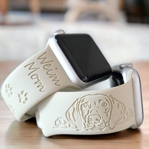 May include: Two white Apple Watch bands with engraved designs. One band has the words "Weim Mom" and paw prints. The other band has an engraved image of a Weimaraner dog.