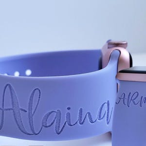 May include: A lavender silicone watch strap with the name "Alaina" engraved on it. The strap is designed for an Apple Watch and has a rose gold finish.