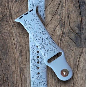 May include: Two gray Apple Watch bands with a science theme. The bands are covered in small black illustrations of science-related items, such as beakers, test tubes, atoms, and light bulbs.